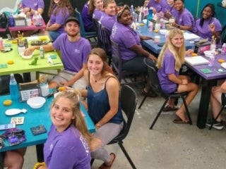a group of students sitting in a crafting room with colorful table