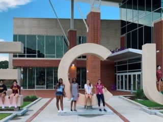 Students in front of the giant ECU sign, some sitting on the letter and some standing in front of the letters.
