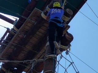 A student climbing up the rope to a high wooden structure