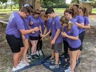 A group of students is standing on a twisted tarp on the ground