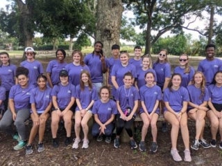 A group of students sitting on long bench under a tree