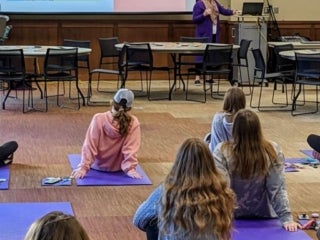 A group of students sitting on yoga mats listening to lecture on projector